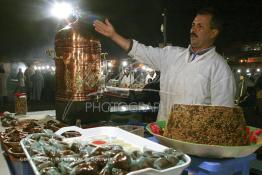 Image du Maroc Professionnelle de  Vendeur de Khoudenjale, une infusion tonifiante constituée de plusieurs herbes aromatiques : elle réchauffe et ouvre l’appétit, aphrodisiaque se prend avant ou après repas. sur la place Jamaa El Fana plusieurs vendeurs de cette tisane sont installés sur la place, ils la proposent avec une sorte de farine cuite mélangées aux amandes, graines de sésames, cacao… Une atmosphère un peu magique dans ces lieus au centre de Marrakech, le 1er Mars 2004. (Photo / Abdeljalil Bounhar)

